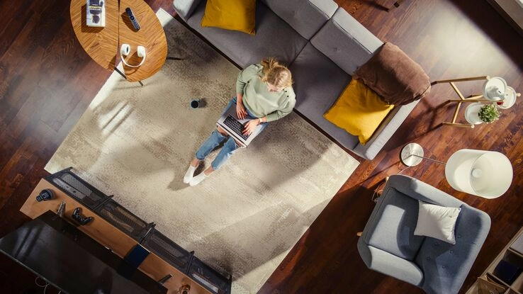 Eine Frau sitzt in ihrem Wohnzimmer auf der Couch. Der Laptop ist auf dem Schoß und sie informiert sich über Versicherungen.