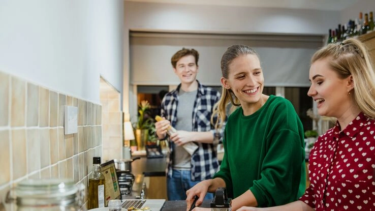 WG-Mitbewohner kochen gemeinsam in der Küche während sie sich unterhalten.