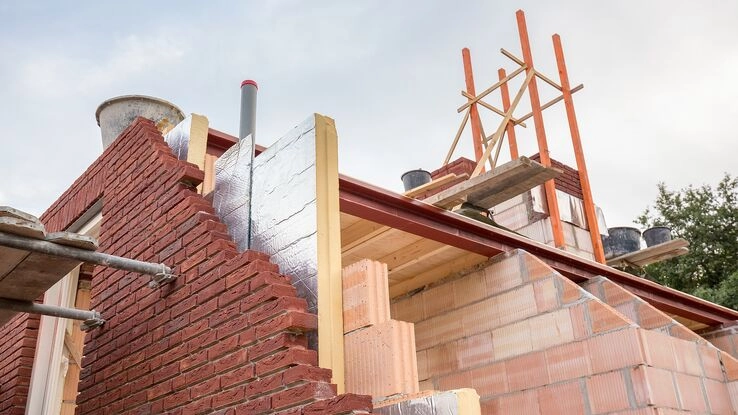 Eine Dämmplatte schaut zwischen Ziegeln und der Innenwand, von einem Haus im Aufbau, hervor. 