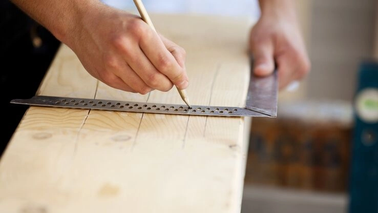 Das Foto zeigt ein Holzbrett und die Hände eines Handwerkers. Ein Symbolbild für Reparaturen von Beschädigungen.