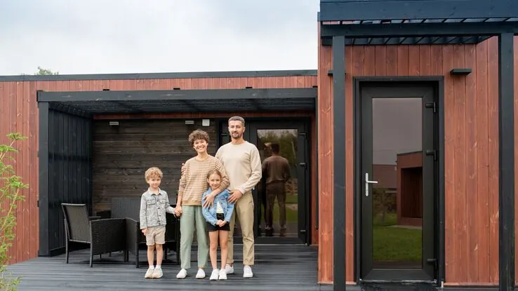 Eine Familie steht vor ihrem festehendem Mini Haus. Dies wird auch Tiny House genannt.