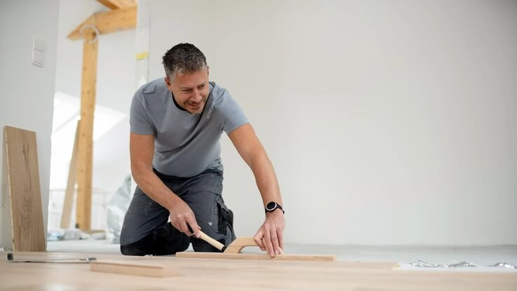 Ein Mann mittleren Alters beim Verlegen von Parkett in einem neuen Dachgeschoss.