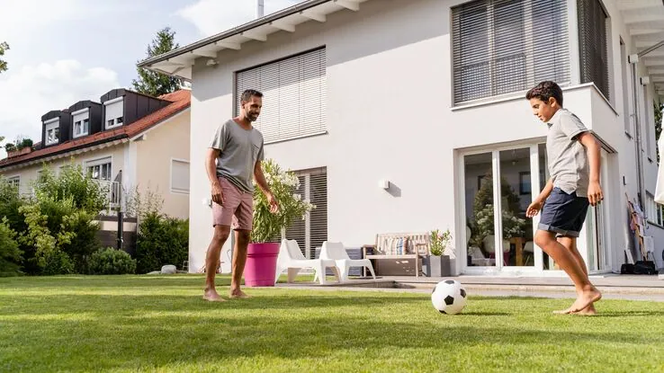 Ein Vater spielt mit seinem Sohn Fußball im Garten.