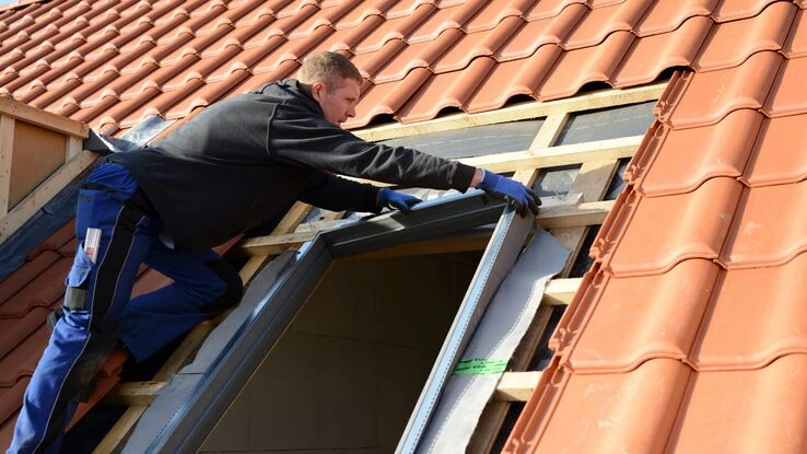 Das Foto zeigt einen Handwerker der ein Fenster erneuert und symbolisiert das Thema energetische Sanierung.