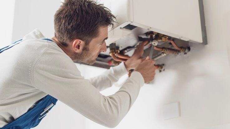 Ein junger Handwerker kontrolliert den Heizboiler und schraubt daran.