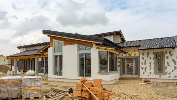 Ein neues Haus wird gebaut. Man sieht zum Teil noch Baumaterialien im Garten sowie noch fertig zu stellende Wände.