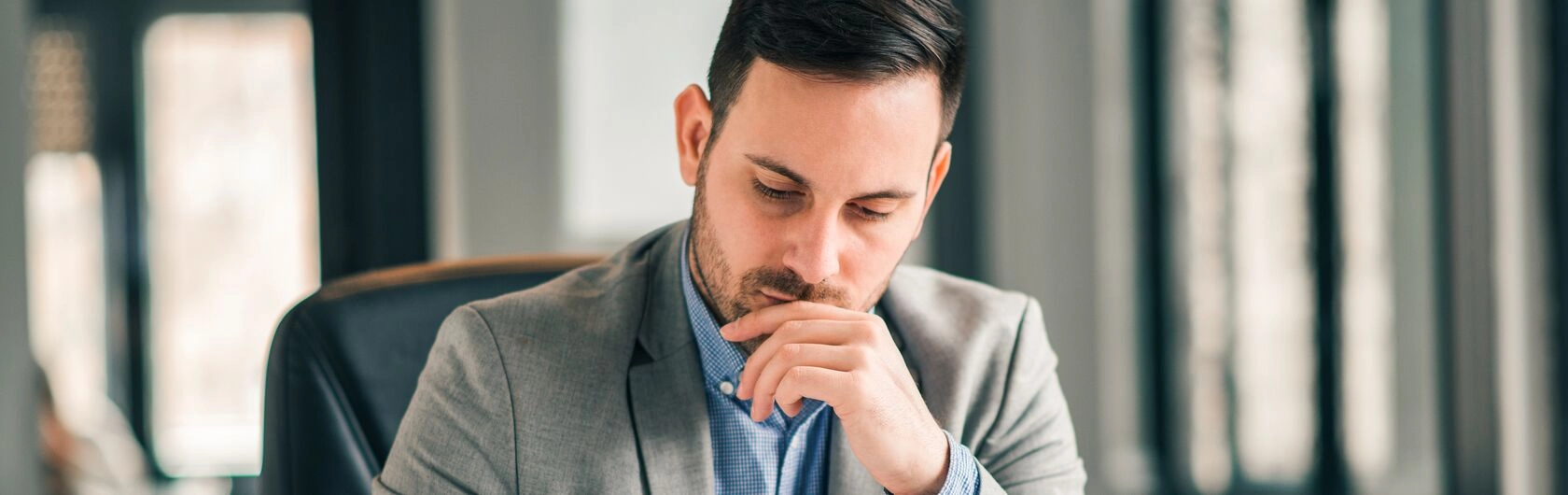 Ein Mann sitzt am Schreibtisch, sein Blick geht überlegend nach unten.