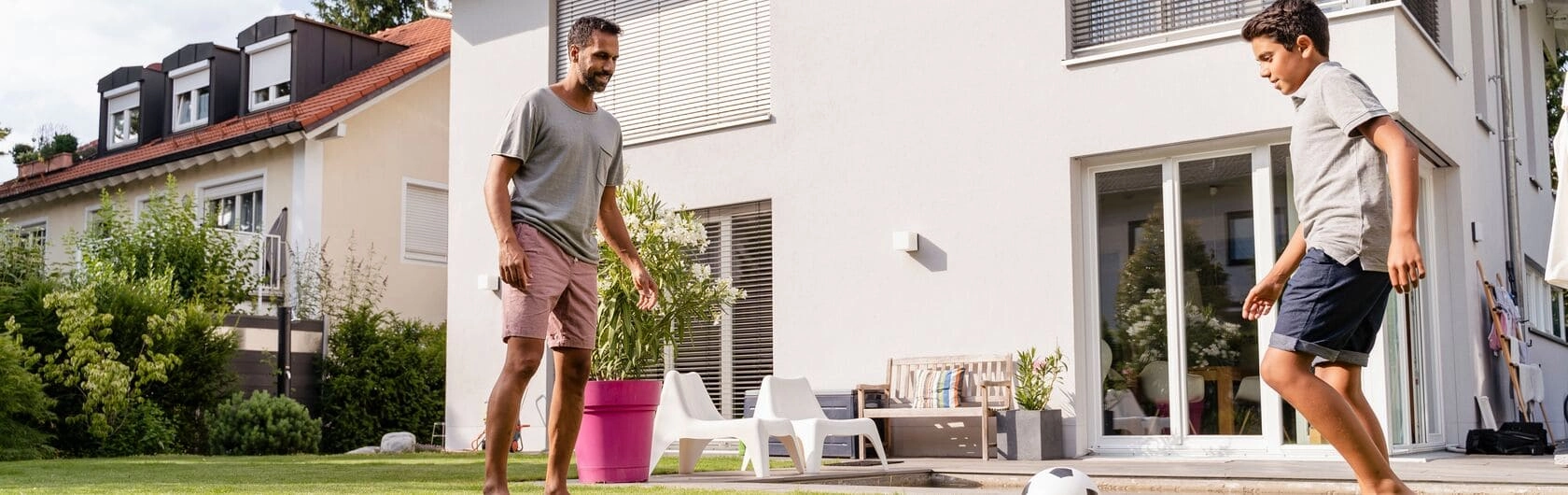 Ein Vater spielt mit seinem Sohn im Garten Fußball.