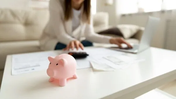 Ein Sparschwein mit einer Frau mit Taschenrechner im Hintergrund als Symbol für Kosten